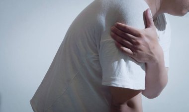 Beyaz gömlekli bir adam kolunu acı içinde tutuyor ve rahatsızlık veriyor. Bu görüntü sağlıkla ilgili temalar, kol yaralanmaları, kronik ağrı ve tedavi aramanın önemi için idealdir..
