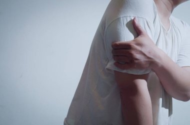 Beyaz gömlekli bir adam kolunu acı içinde tutuyor ve rahatsızlık veriyor. Bu görüntü sağlıkla ilgili temalar, kol yaralanmaları, kronik ağrı ve tedavi aramanın önemi için idealdir..