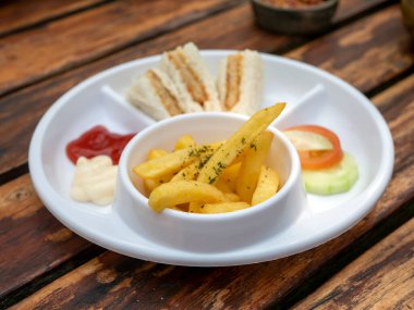 Taze dilimlenmiş hamburgeri ve patates kızartmasını ahşap masada beyaz tabakla kapat..