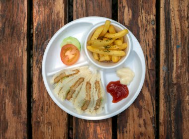 Taze dilimlenmiş hamburgeri ve patates kızartmasını ahşap masada beyaz tabakla kapat..