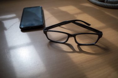 Gözlüklü ve akıllı telefonlu bir iş masası. Kopyalama alanı olan tahta arkaplan.