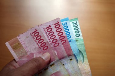 Yetişkin parmağı Rupiah 'ı tutuyor, Endonezya parası ve bulanık kahverengi bir geçmişi var. Kaydetme ve verme konsepti