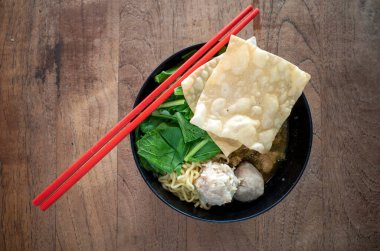 Mie Pangsit Bakso, taze sebzeli bir kase köfte çorbası ve eski ahşap masada kırmızı çubuklar..
