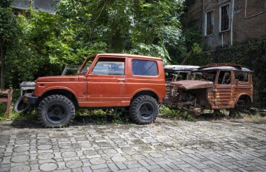Eski kırmızı bir araba ve tekerlekleri olmayan paslı eski nesil bir araba..