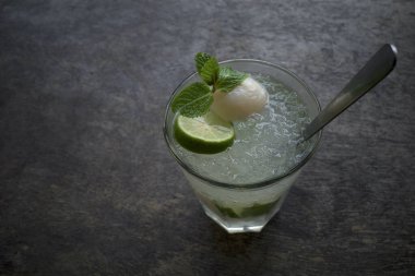 Bir bardak limonlu su, likör, dilimlenmiş limon ve nane yapraklarıyla süslenmiş eski ahşap bir masa..