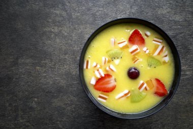 Eski ahşap bir masada, mango, kivi ve çilekli tropikal bir meyve suyu kasesi..