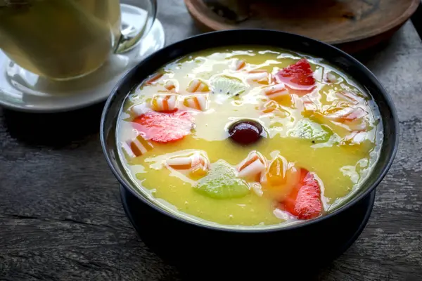 Eski ahşap bir masada, mango, kivi ve çilekli tropikal bir meyve suyu kasesi..