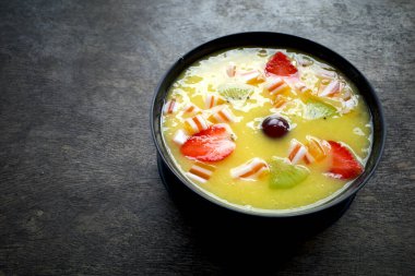 Eski ahşap bir masada, mango, kivi ve çilekli tropikal bir meyve suyu kasesi..