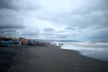 Depok Sahili, Yogyakarta, Endonezya 'daki bulutlu arka planda ziyaretçiler ve balıkçı tekneleri..
