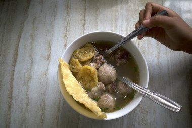 A bowl of meat ball soup with fresh vegetables on the old wooden table.