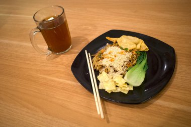Mie Pangsit Bakso, taze sebzeli bir kase köfte çorbası ve eski ahşap masada bir bardak çay..