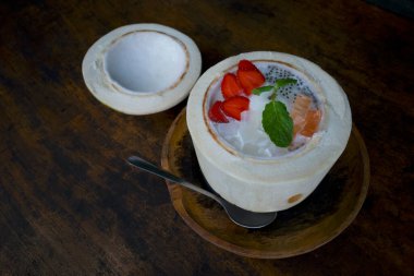 Karışık meyve salatası, koyu ahşap bir masanın üzerinde taze hindistan cevizli renkli bir tatlı..