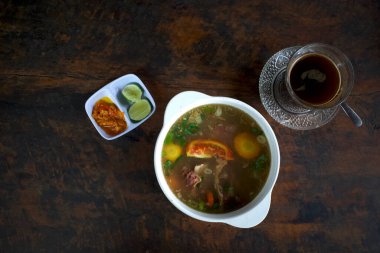 Taze sebzeli bir kase et çorbası dilimlenmiş biber, dilimlenmiş limon ve eski ahşap masada bir bardak sade kahve..
