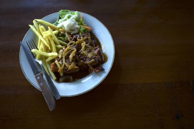 Beyaz tabakta dilimlenmiş tavuk bifteği, sebze ve patates kızartması, eski, ahşap bir masada..