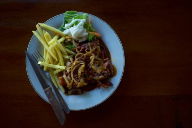 Beyaz tabakta dilimlenmiş tavuk bifteği, sebze ve patates kızartması, eski, ahşap bir masada..