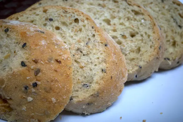 Tam buğday ekmeği, tohumlu, beyaz tabakta kesilmiş, sağlıklı ekmek seçimi..