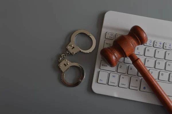 Judge gavel, laptop keyboard and handcuffs isolated on a grey background. Copy space for the text. Online scam, fraud, arrest and criminal concept.