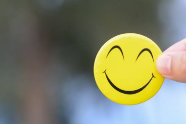 Gülümseyen bir yüzü tutan bir el, olumlu bir zihniyeti, yapıcı geri bildirimi, hayata neşeli bir yaklaşımı ve sağlıklı bir yaşam tarzına olan bağlılığı simgeler..