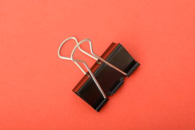 Ataç kırmızı arkaplanda izole edilmiş. Bir ataç, kağıtları bir arada tutmak için tasarlanmış basit ama dahice bir ofis aracıdır.