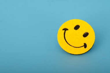 Mavi arkaplanda gülen surat ifadesi, pozitiflik ve neşe dolu duygular taşıyor.