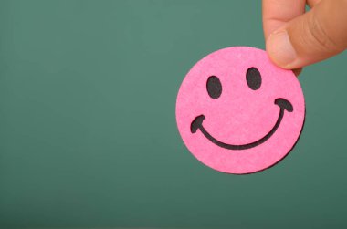 Gülen suratlı bir elin tasviri pozitifliğin etkisini vurgular ve neşeli bir perspektifin genel refahı ve hayattan memnuniyeti artırabileceğini öne sürer..