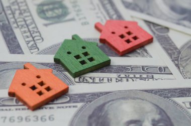 Arka planda para banknotları olan bir ev imajı gayrimenkul varlıklarına bağlı zenginliği sembolize eder..