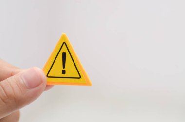 Sarı uyarı levhasını tutan bir el, çeşitli durumlarda dikkat ve farkındalığın önemini vurgulayarak bireylere dikkatli ve potansiyel risklere karşı hazırlıklı olmaları gerektiğini hatırlatır.