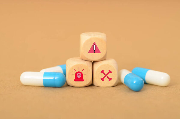 wooden block with symbols of an exclamation point, a siren, a skull and crossbones, and capsules visually represents the potential dangers and consequences associated with medication misuse.