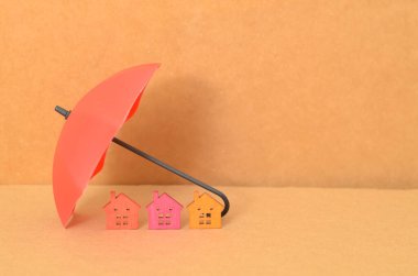 Üç minyatür evi barındıran kırmızı şemsiye, ev sigortasının sağladığı koruma ve güvenliği simgeliyor..