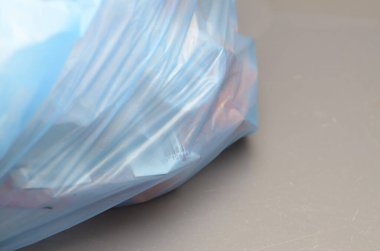 Sıkıca bağlanan mavi plastik çizgileriyle, daha büyük bir çevresel sorunun geçici bir çözümü olan atıkları kapsamayı sembolize ediyor..