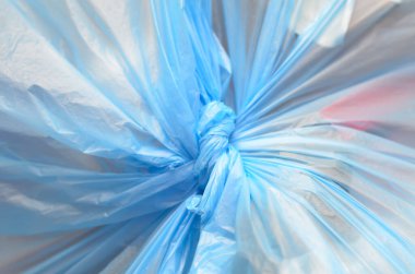 Sıkıca bağlanan mavi plastik çizgileriyle, daha büyük bir çevresel sorunun geçici bir çözümü olan atıkları kapsamayı sembolize ediyor..