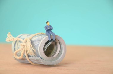 Bir yığın para banknotunun tepesinde oturan işadamı derin düşüncelere dalmış mali kazanç için bir sonraki hedefini planlıyor..