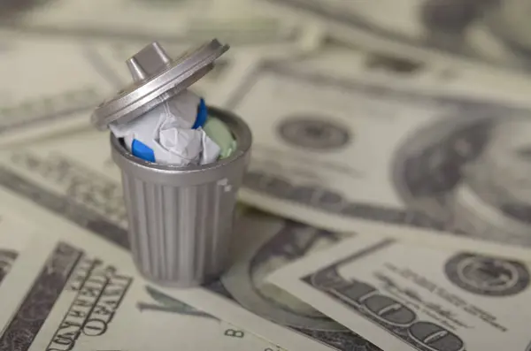 stock image The image depicts a miniature trash can filled with crumpled paper money, symbolizing the concept of wasted money or financial loss.