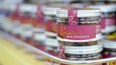 Langkawi, Malezya: 2 Ekim 2024: Süt çikolatasıyla kaplanmış kuru üzüm dolu cam kavanozlar bir rafta sergileniyor.