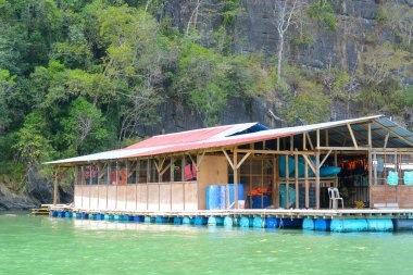 Platformda birkaç mavi varil var, muhtemelen depolama veya balıkçılık ekipmanları için kullanılıyor..