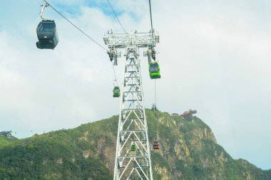 Bir teleferik sistemi sarp bir dağa tırmanıyor ve çevresindeki manzaranın nefes kesici manzarasını sunuyor..