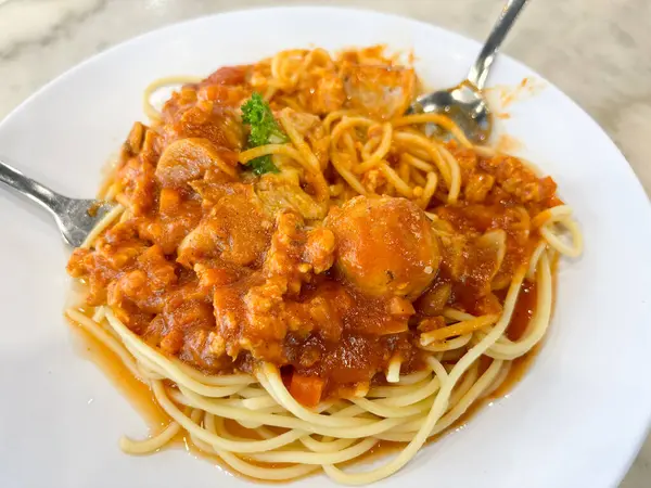 Kalın, kırmızı domates soslu bir tabak spagetti iki çatalla servis edilir..