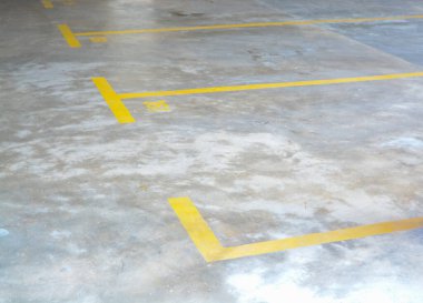 Görüntü, park yerlerini işaretleyen sarı çizgili beton bir otoparkı gösteriyor..