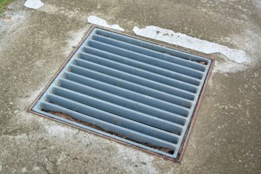 Görüntü beton bir yüzeye gömülmüş metal bir ızgarayı gösteriyor..