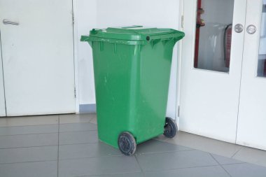 Görüntü, beyaz bir kapının yanına yerleştirilmiş yeşil bir tekerlek kutusunu gösteriyor..