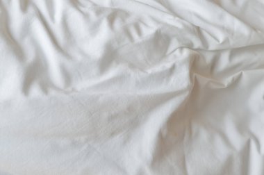 Görüntü, beyaz bir yatak çarşafının, buruşuk ve desenli bir yakın çekimini gösteriyor..