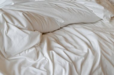 Görüntü, beyaz bir yatak çarşafının, buruşuk ve desenli bir yakın çekimini gösteriyor..