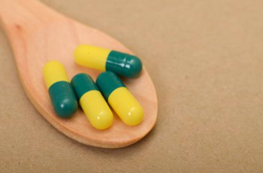 Birkaç yeşil ve sarı kapsül, ahşap bir kaşığa düzgün bir şekilde yerleştirilmiş. Bu da sağlık ve sağlığa odaklandığını gösteriyor..