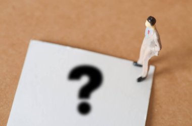 Takım Elbiseli Minyatür Adam Devasa Soru İşareti 'nin önünde duruyor. Belirsizlik ve Yansımayı simgeliyor.