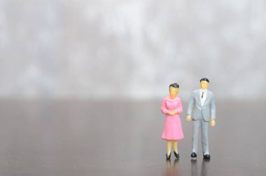 Gri takım elbiseli minyatür adam ve profesyonel bir ikiliyi temsil eden pembe elbiseli kadın.