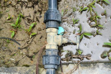 Eski paslı kablolar tarafından tutulan çürüyen bir boru uyumu, yaşlanan su sistemleri ve potansiyel altyapı arızası için güçlü bir görsel metafor görevi görmektedir..