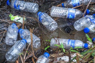 Klang, Malaysia: October 7th 2025 - Discarded single-use water bottles with blue caps pollute a muddy ditch, starkly illustrating the devastating environmental impact of plastic waste on natural habitats.