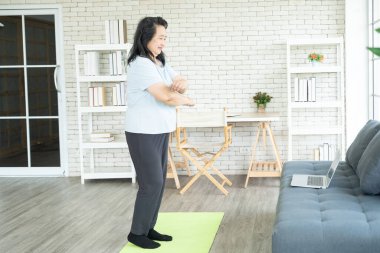 Kıdemli Asyalı bayan kollarını egzersizle ya da spor yaparak evdeki bilgisayardan VDO 'yu takip ederek sallıyor. Sağlık bilinci olan yaşlı insanlar kavramı..