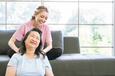 Asyalı anne, tatlı Asyalı kızının koltuğa oturup masaj yapması ve yaşlı Asyalı annenin evde çektiği acıyı hafiflettiği için mutlu..