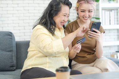 Yaşlı yaşlı bayan kredi kartıyla online alışveriş yaparken tatlı kızına yardım ediyor ya da ona katılıyor. Aile kavramı ile evde online alışveriş.